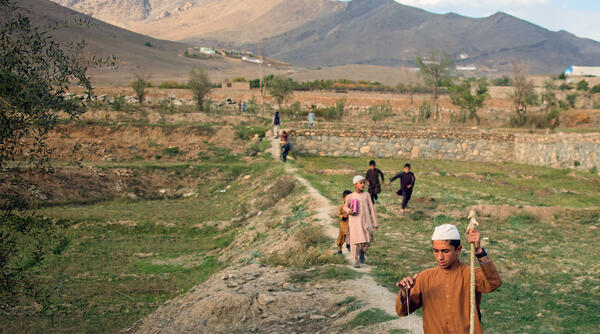 Boys walking across a field and mountains in Afghanistan